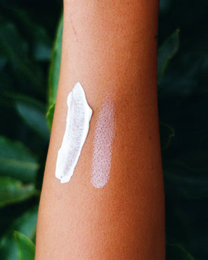 Close-up of a person's arm with a small amount of white cream applied against a dark green leafy background
